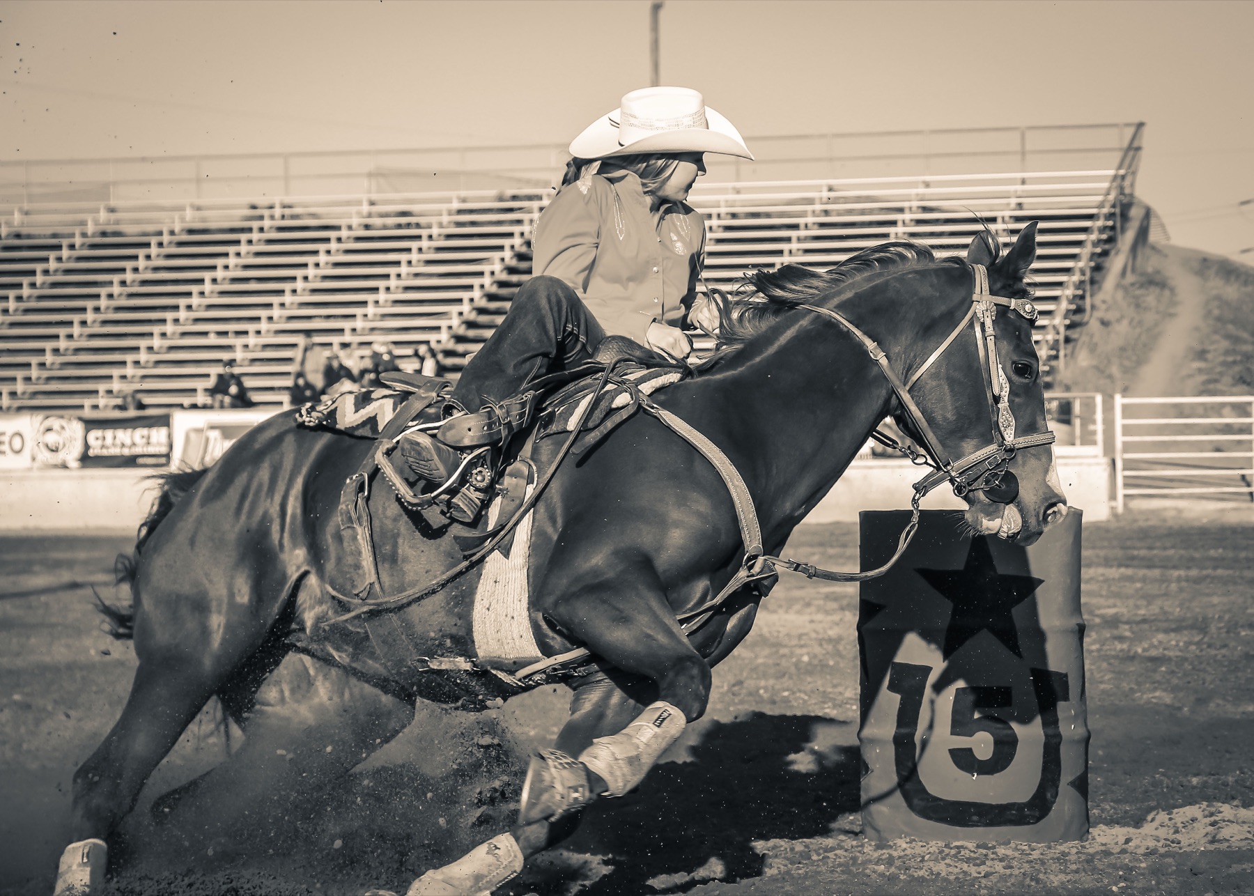 Cowgirl on horseback rounding a barrel during a rodeo barrel racing run